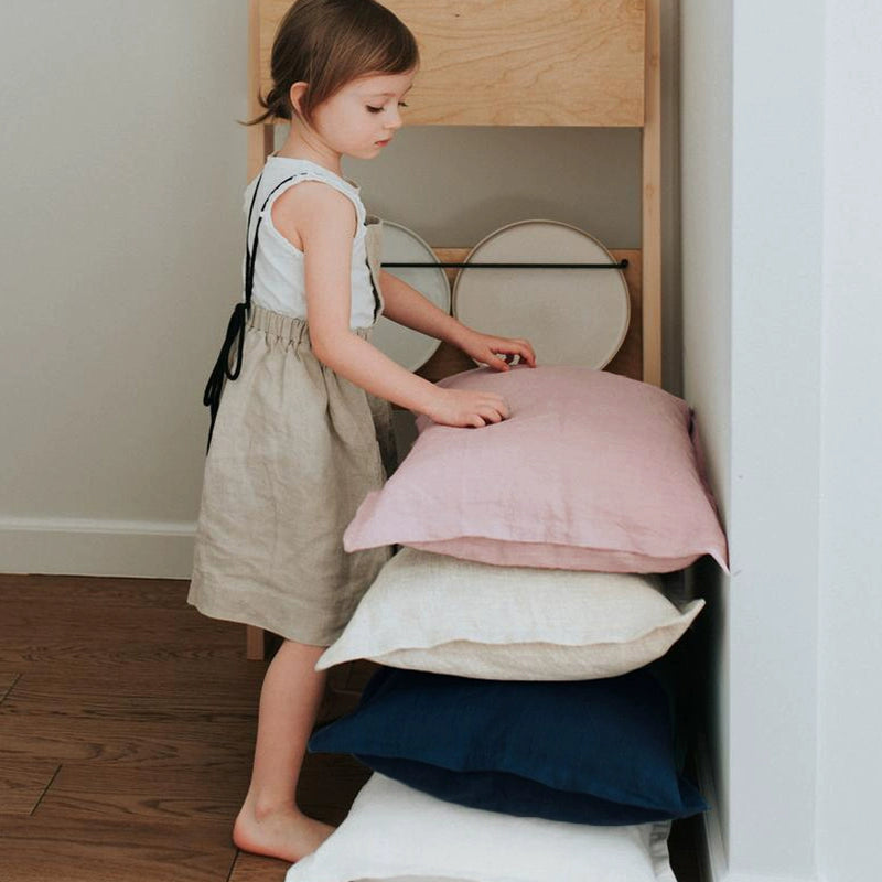 Stack of elegant linen pillow cases in pink, cream, navy, and white, with frills.